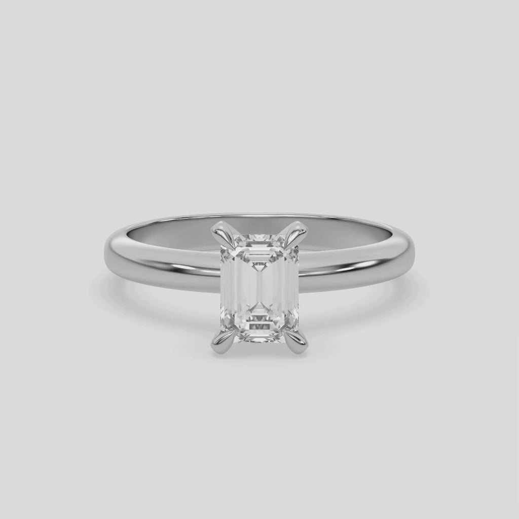 This video features a white gold ring features an emerald solitaire diamond elegantly secured in a four-prong setting on a solid gold band 