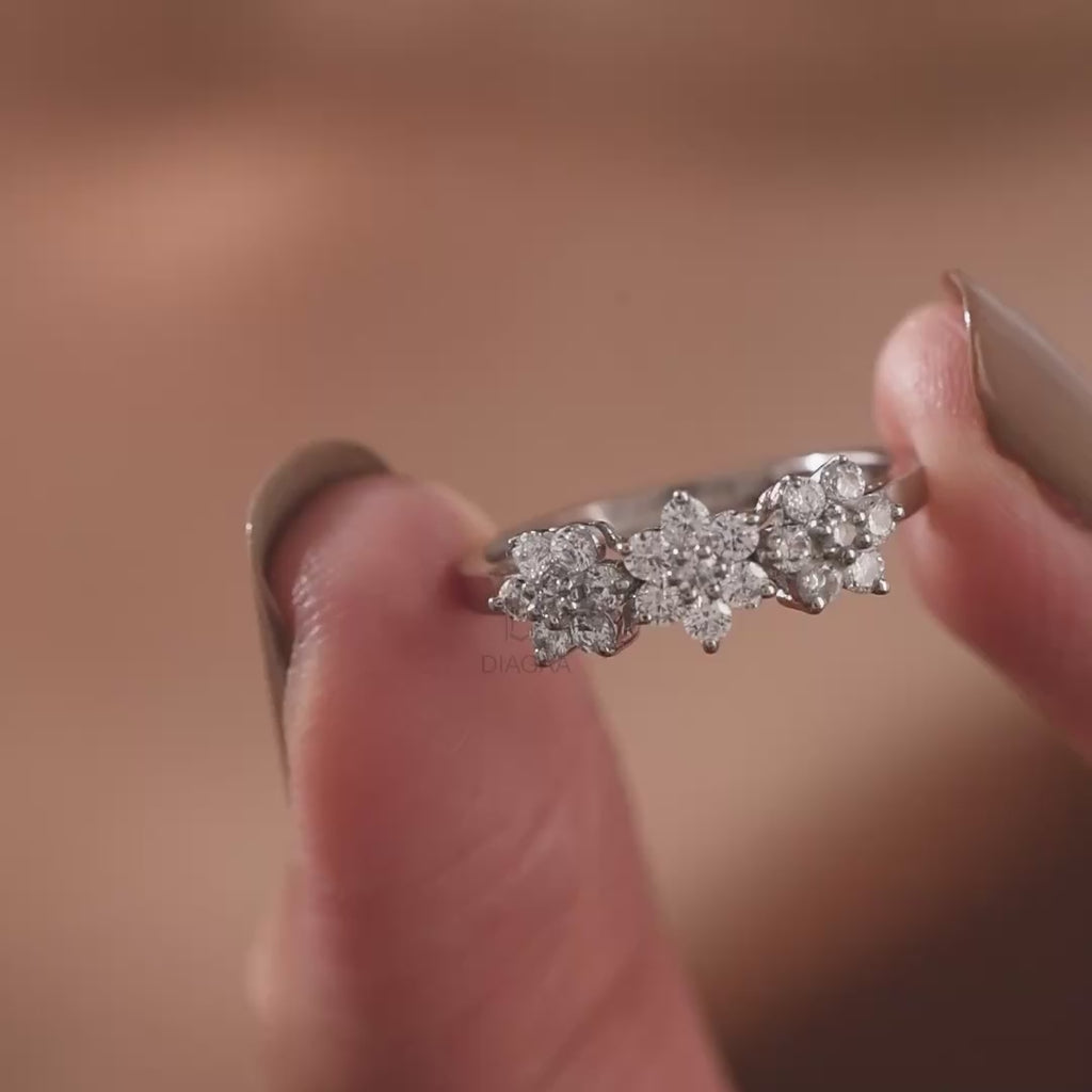 Video of a hand holding and wearing a delicate white gold diamond ring featuring a sparkling three-flower cluster design.