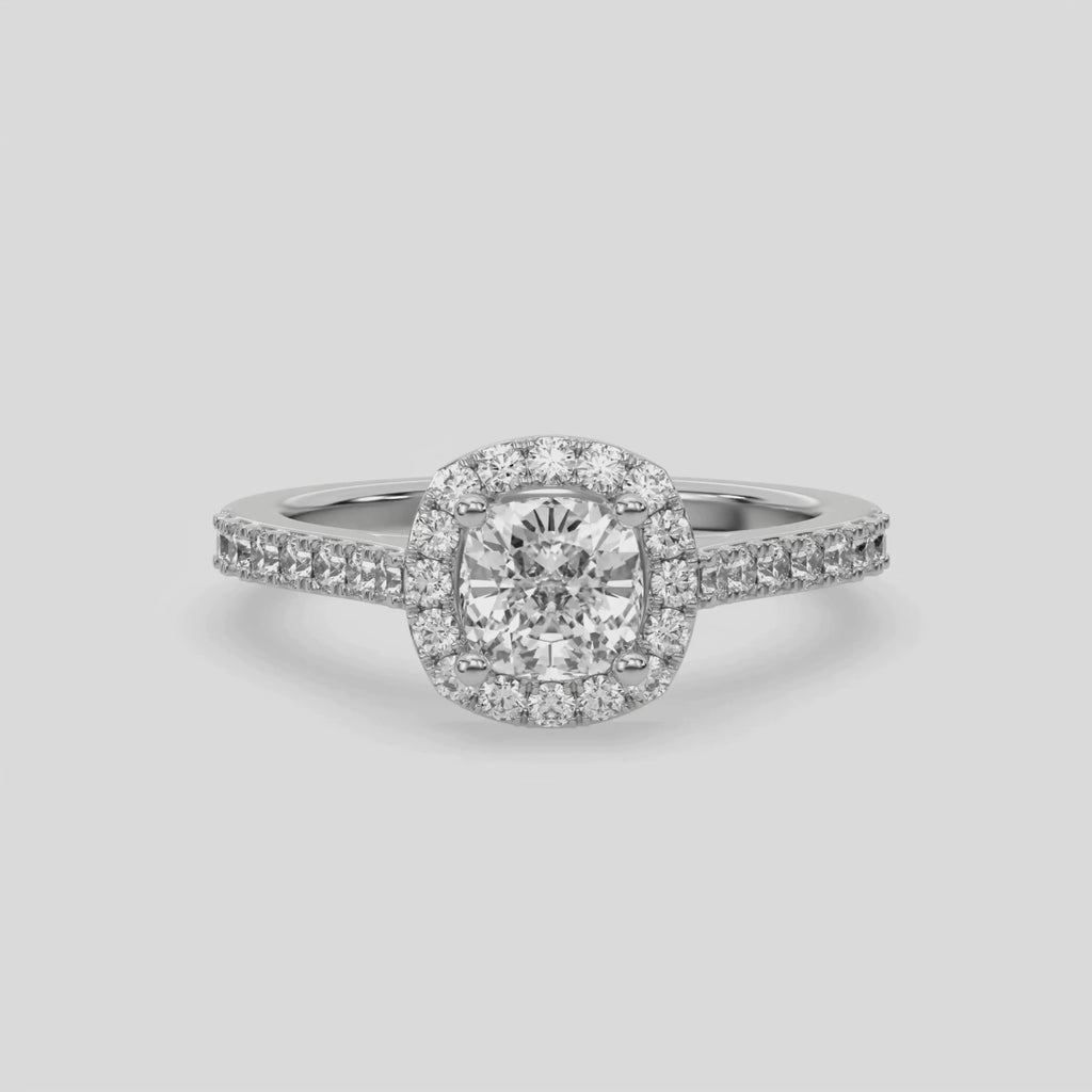 This video features a white gold Cushion Diamond Halo Engagement Ring is made with a cushion solitaire diamond set in a four-prong setting, surrounded by a halo of round diamonds all set on a pave band 