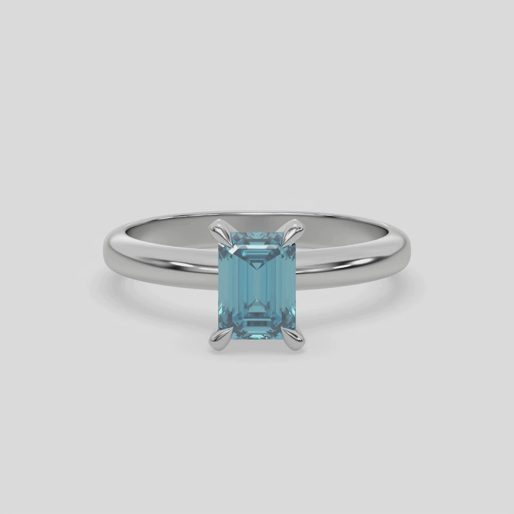 This video features a white gold ring features an fancy Blue emerald solitaire diamond elegantly secured in a four-prong setting on a solid gold band 