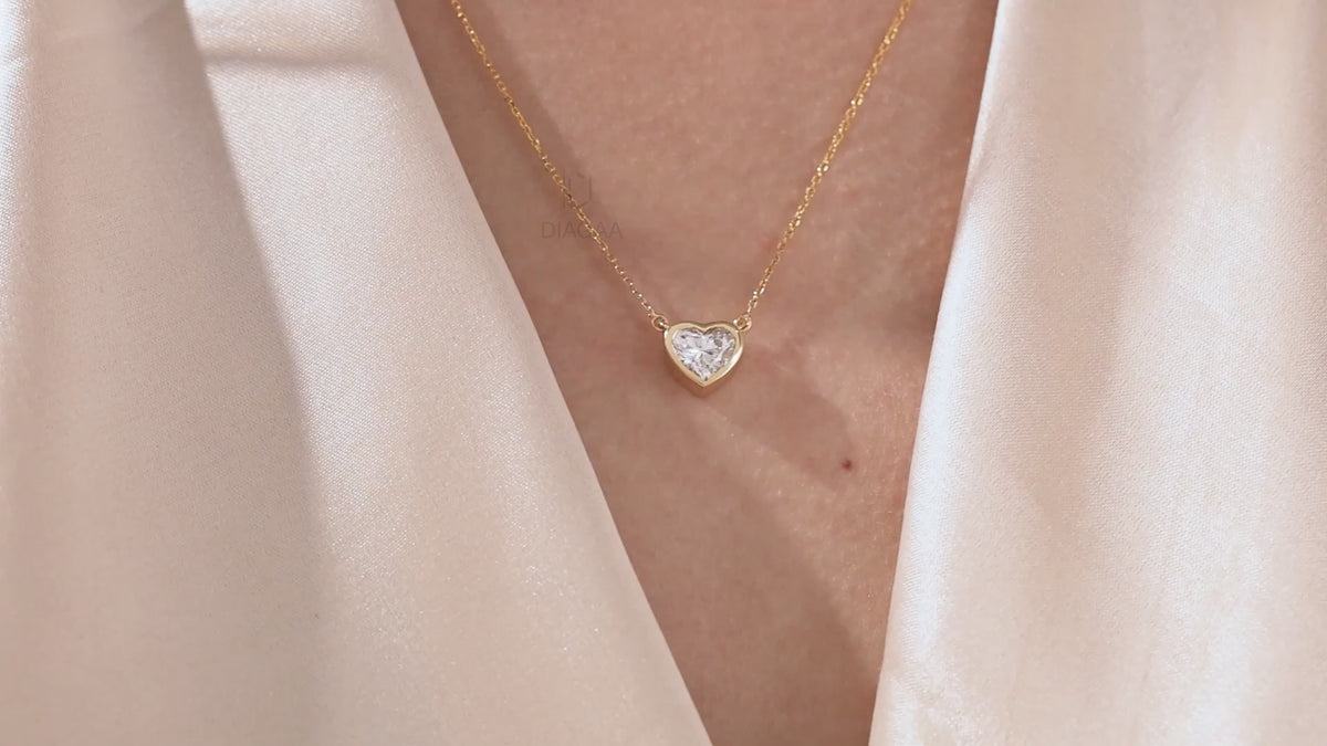 Model wearing a delicate bezel-set heart diamond necklace in yellow gold, featuring a brilliant heart-cut stone on a fine gold chain.