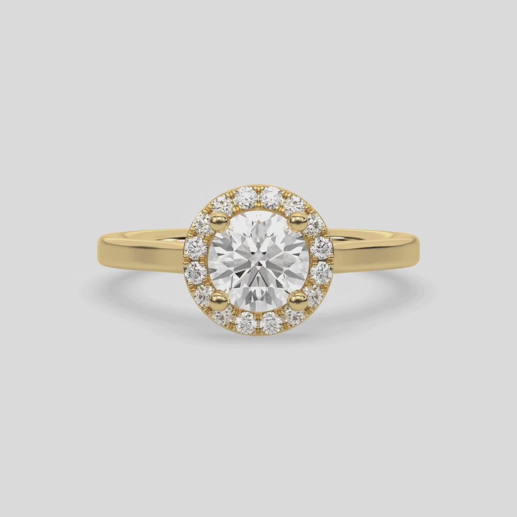 This video features a yellow gold ring features a Round solitaire diamond set in a four-prong setting, surrounded by a halo of round diamonds, all resting on a delicate gold band