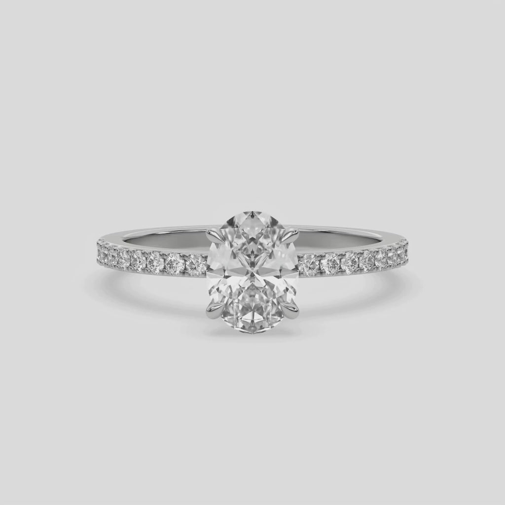 This video features a white gold ring is made with an oval solitaire diamond set in four-prong setting, and is complemented by a round pave diamonds band 