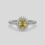 This video features a white gold Oval Diamond Halo Engagement Ring is made with a fancy yellow oval solitaire diamond set in a four-prong setting, surrounded by a halo of round diamonds all set on a pave band