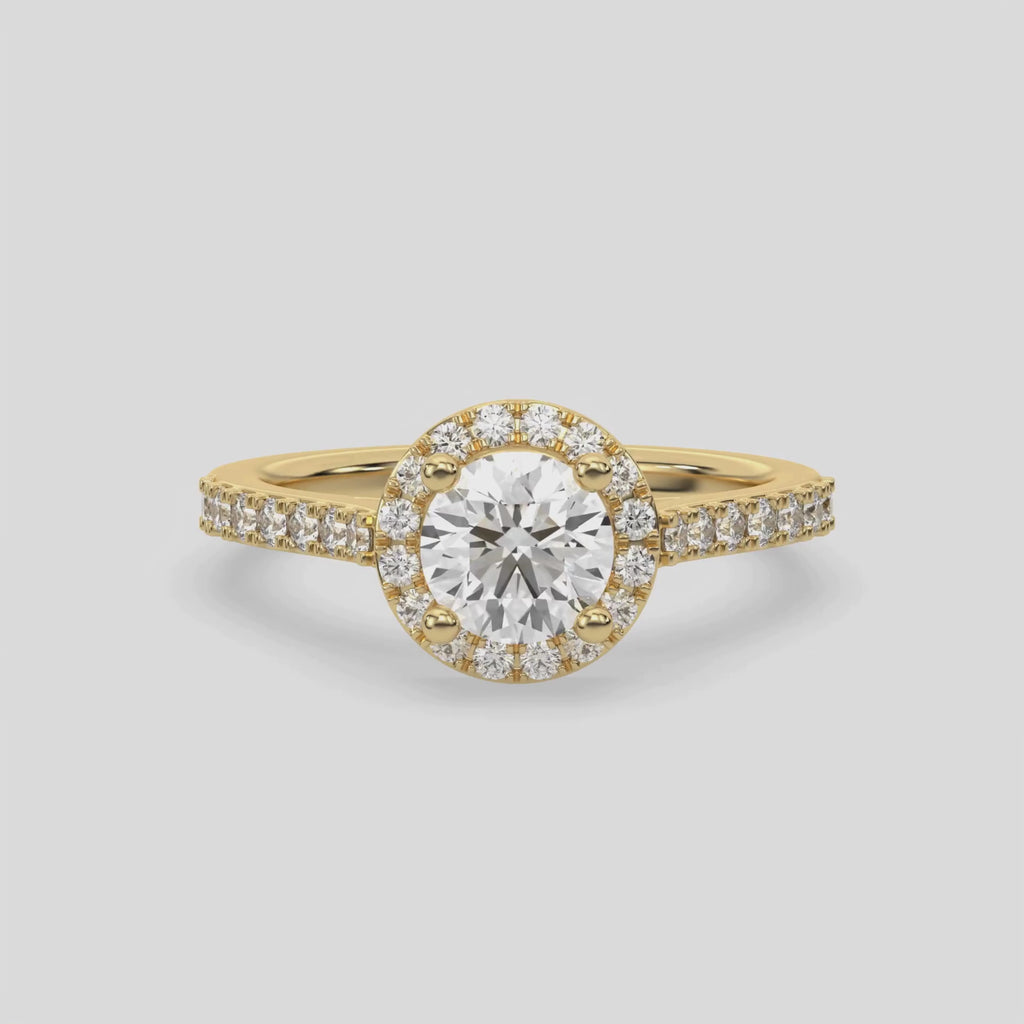 This video features a yellow gold Round Diamond Halo Engagement Ring is made with a round solitaire diamond set in a four-prong setting, surrounded by a halo of round diamonds all set on a pave band 