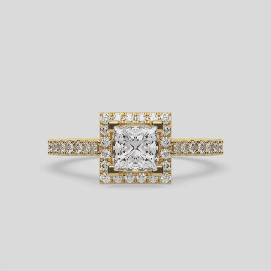 This video features a yellow gold Princess Diamond Halo Engagement Ring is made with a princess solitaire diamond set in a four-prong setting, surrounded by a halo of round diamonds all set on a pave band 