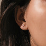 Woman wearing a minimalist princess bezel-set yellow gold stud earring featuring a clear princess-cut cubic earring.