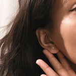 Close-up of a woman wearing a minimalist gold square stud earring with a diamond center. Dainty everyday jewelry on an earlobe piercing.